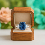 Blue gemstone ring in a wooden box with a blurred floral background