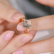 Close-up of a hand wearing a gold ring with a gemstone, blurred background
