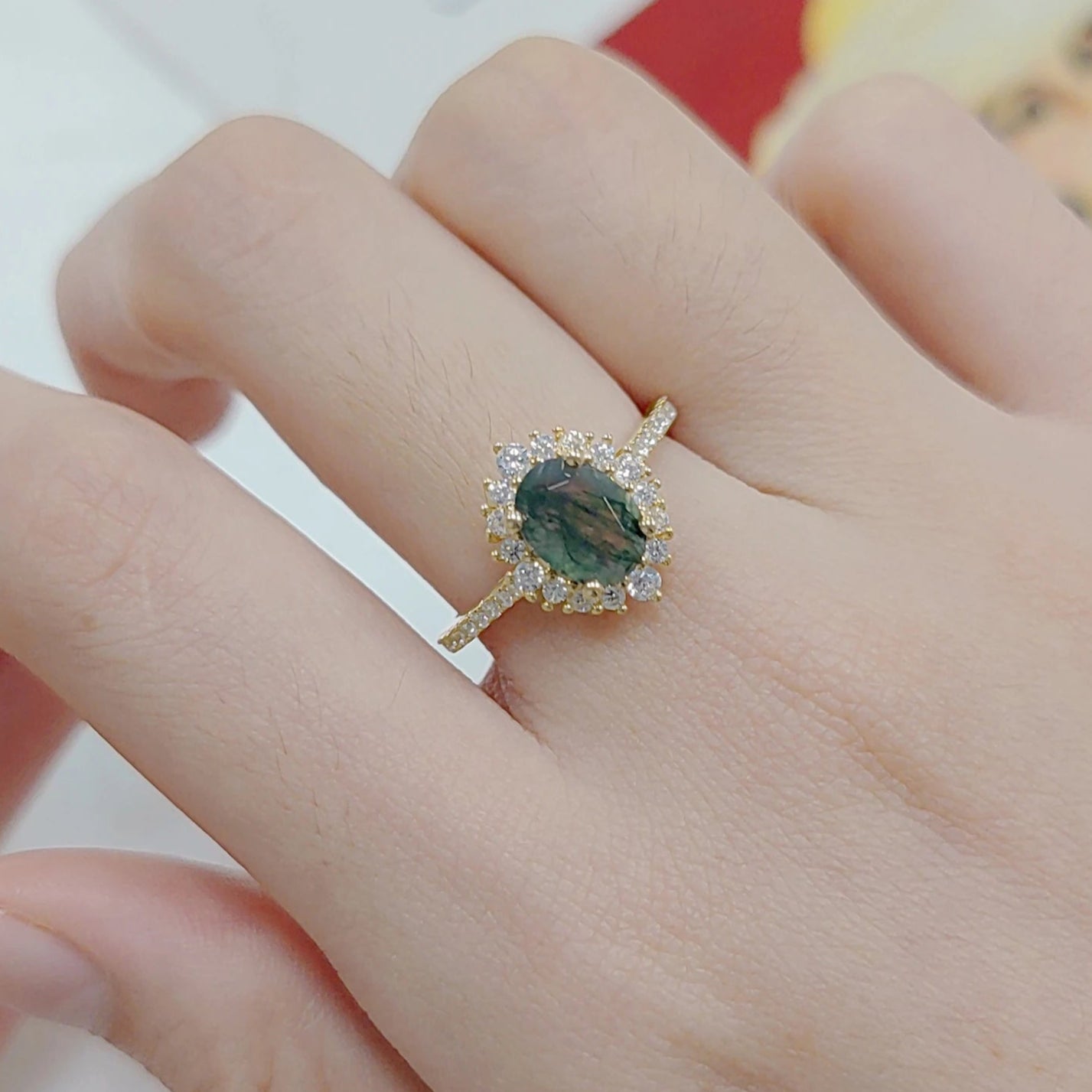 Close-up of a hand wearing a ring with a green gemstone on a blurred background