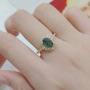 Close-up of a hand wearing a ring with a green gemstone on a blurred background