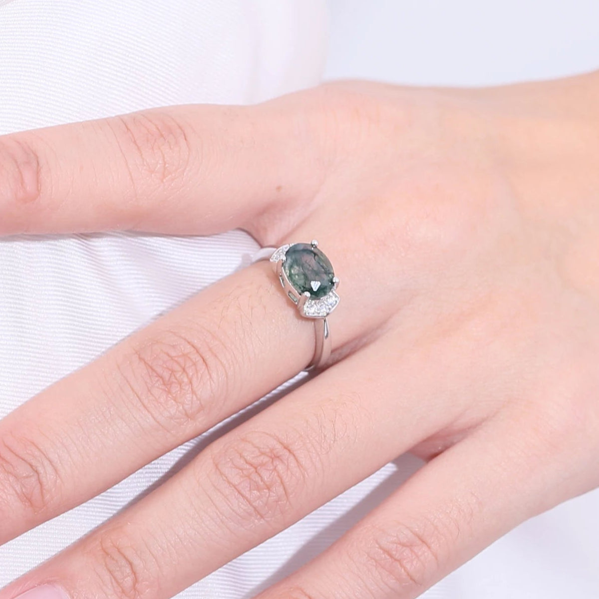 Close-up of a hand wearing a ring with a green gemstone on a white background