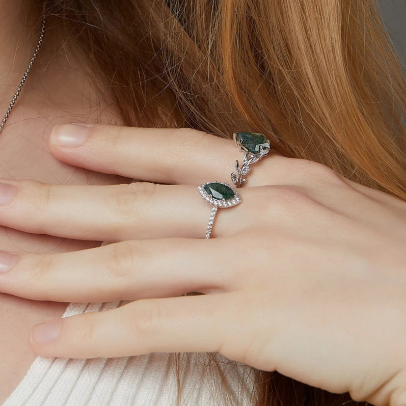 Close-up of a hand wearing a silver ring with a green gemstone, held against a neutral background.