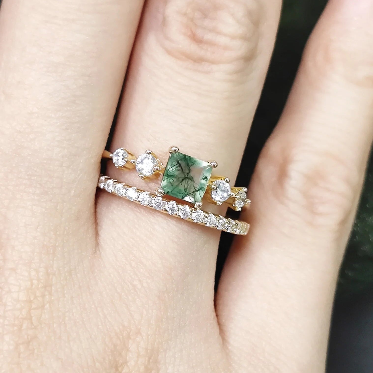 Close-up of a hand wearing two rings with a green gemstone and diamond accents.