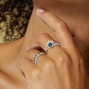 Close-up of a hand wearing two silver rings with green gemstones on a neutral background