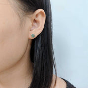 Close-up of an ear wearing a green earring with a light blue background
