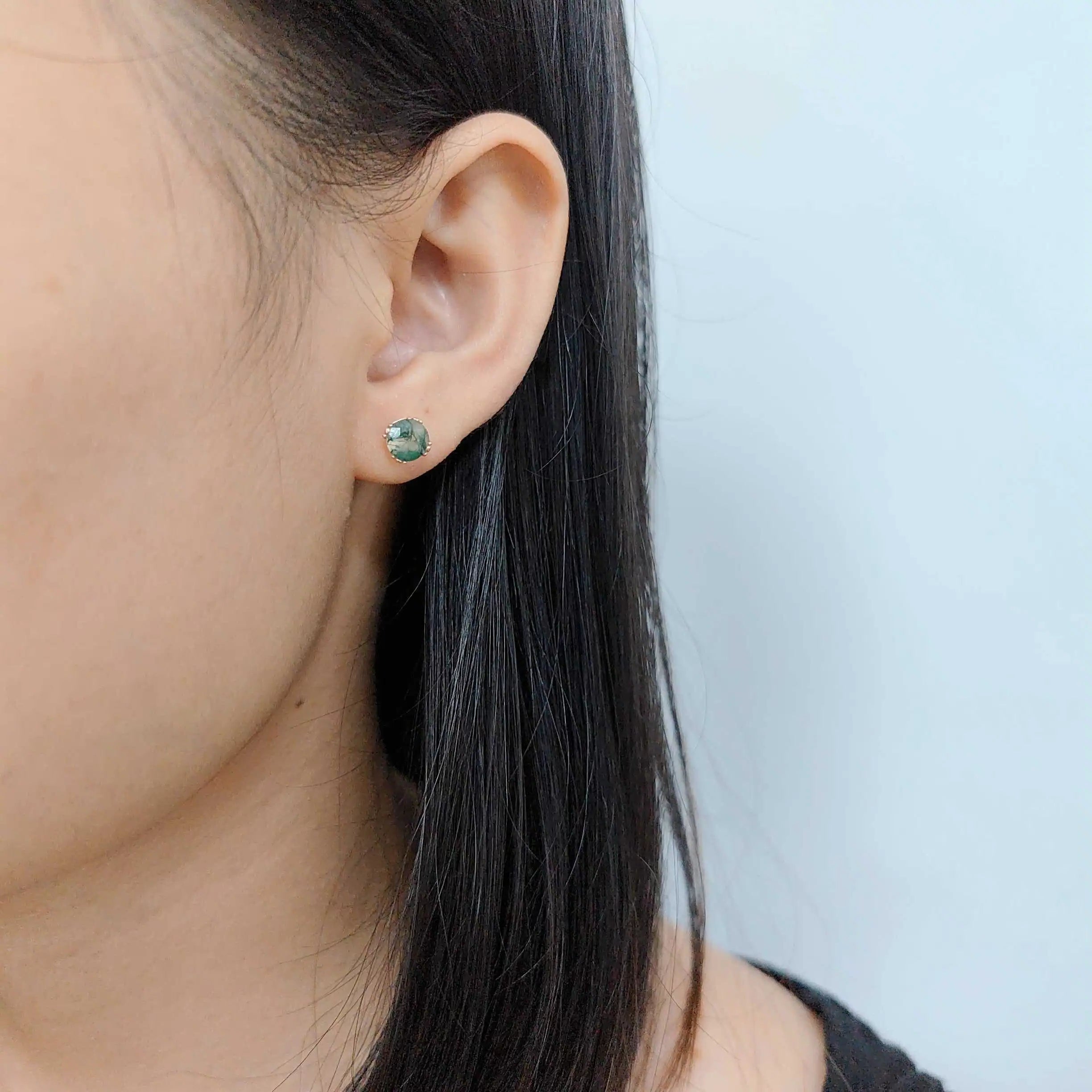 Close-up of an ear wearing a green earring with a light blue background