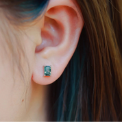 Close-up of an ear wearing a green gemstone earring with blurred hair and background