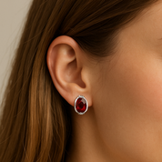 Close-up of an ear wearing a red gemstone earring with a neutral background