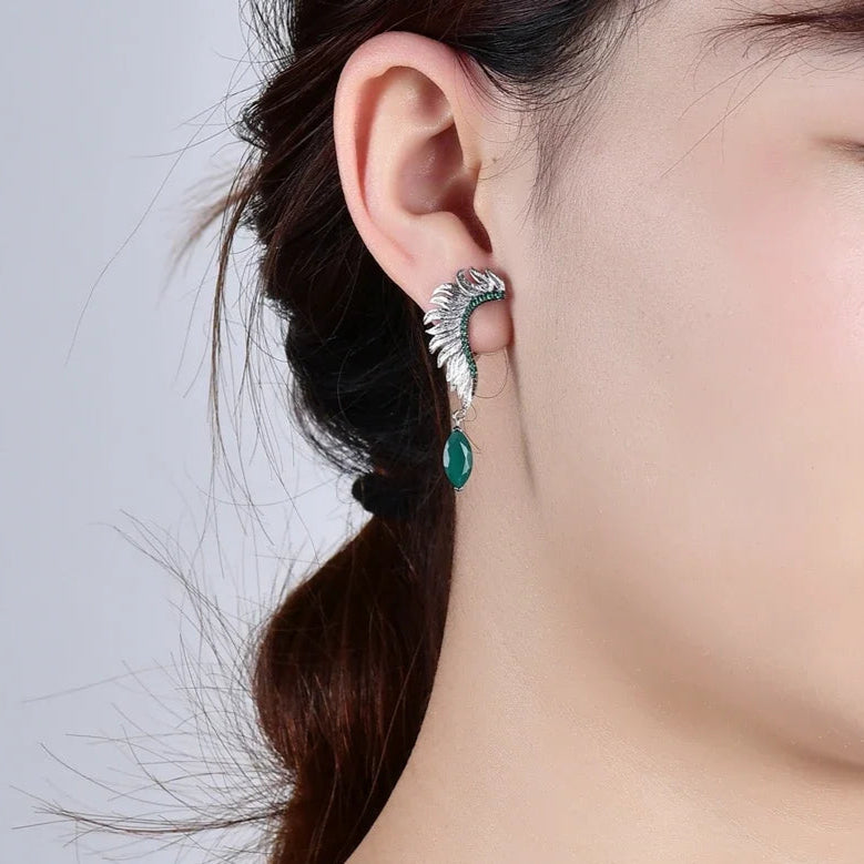 Close-up of an ear wearing a silver earring with a green gemstone on a plain background