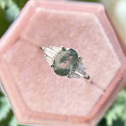 Diamond ring with a green gemstone in a pink velvet box