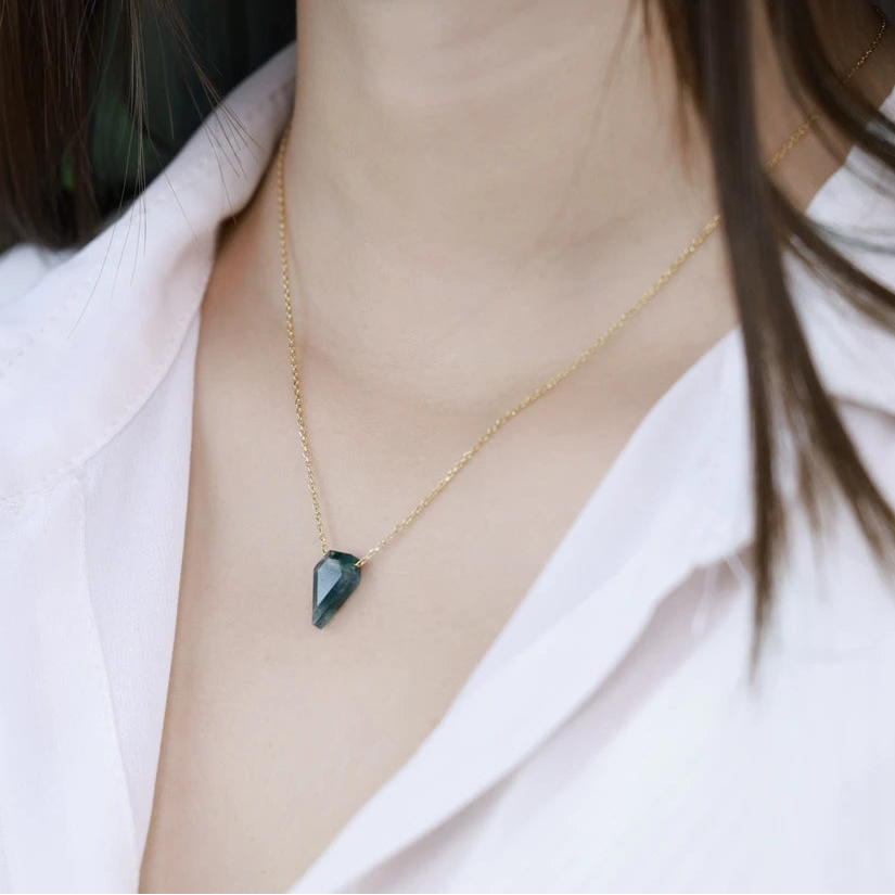 Gold necklace with a green gemstone pendant worn by a person
