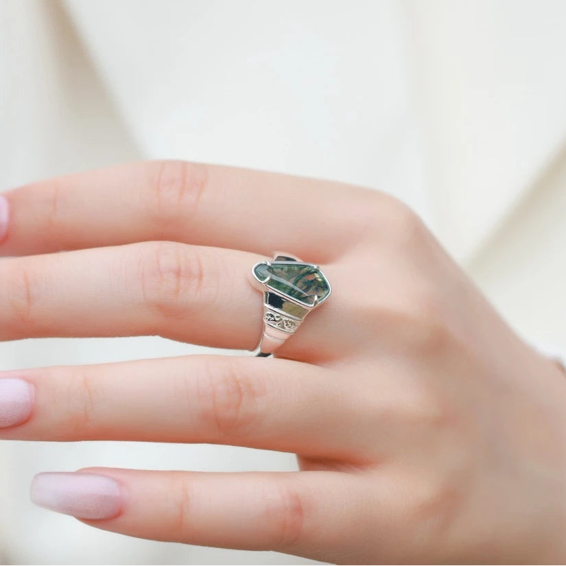 Hand wearing a silver ring with a green gemstone on a light background