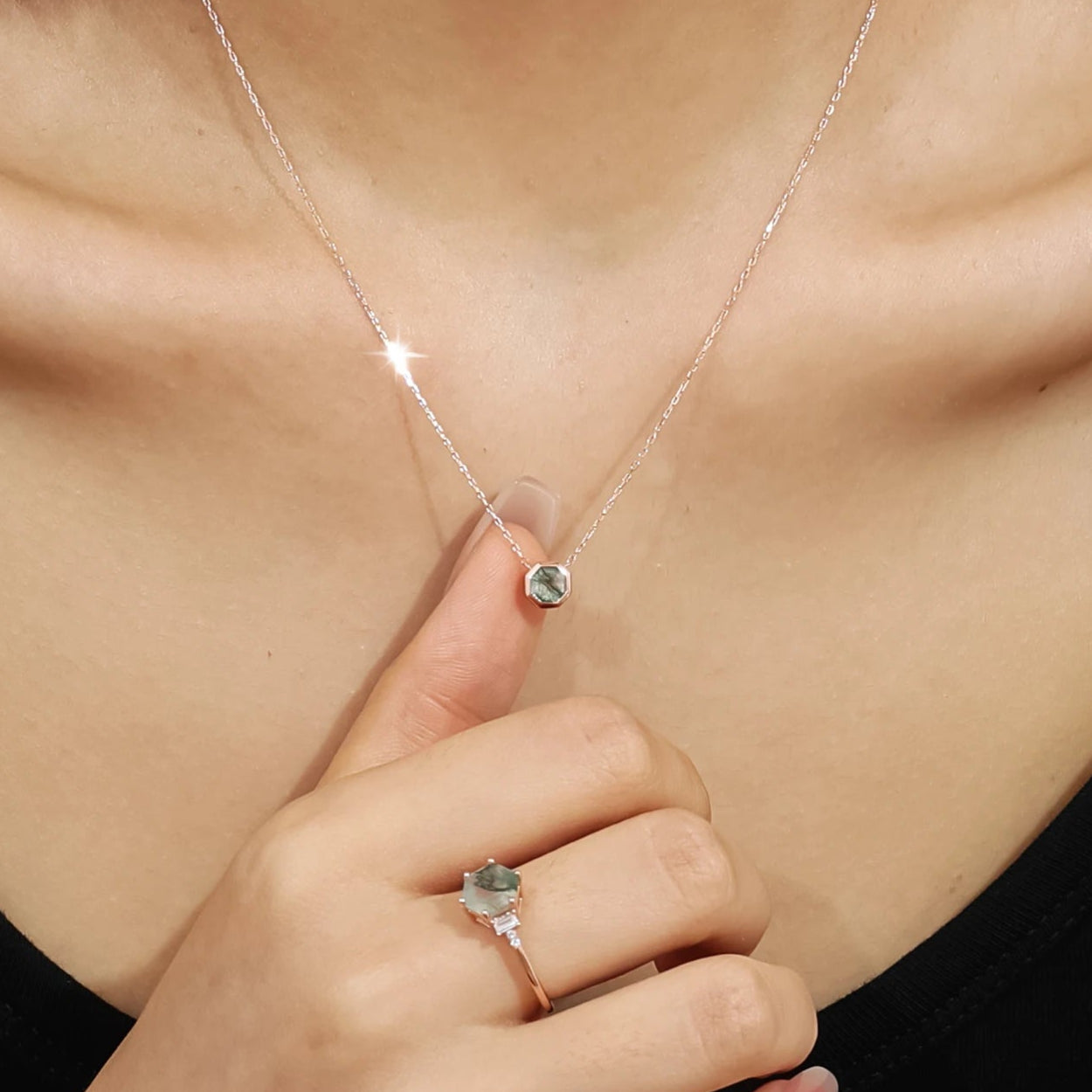 Close-up of a necklace with a pendant and a ring on a person's hand, wearing a black top.