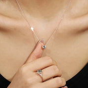 Close-up of a necklace with a pendant and a ring on a person's hand, wearing a black top.