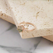 Rose gold ring with a green gemstone on a light stone surface