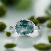 Silver ring with a green gemstone on a light blue background