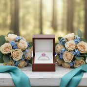 Engagement ring in a box with two bouquets of flowers on a wooden surface in a forest setting.