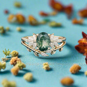 Gold ring with a green gemstone and diamonds on a blue surface with dried flowers in the background