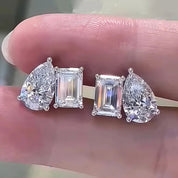 Four diamond earrings on a finger against a neutral background