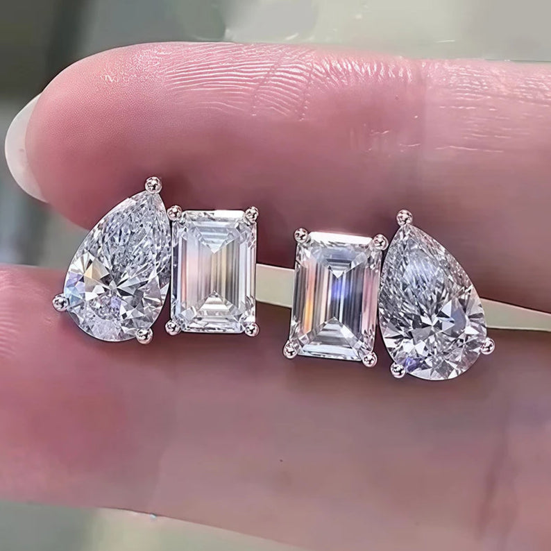 Four diamond earrings on a finger against a neutral background