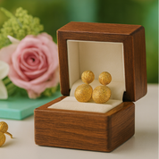 Gold earrings in an open wooden box with flowers in the background