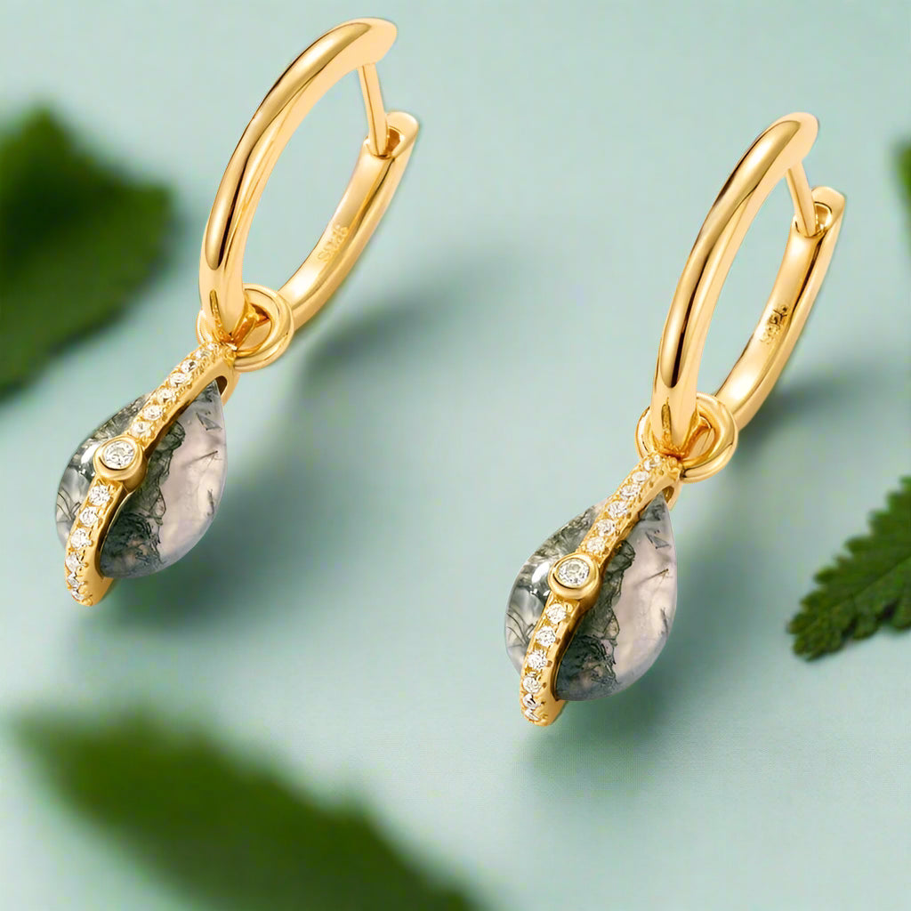 Gold earrings with green teardrop-shaped stones on a light gray background