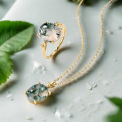 Gold ring and pendant with green gemstone on a light background
