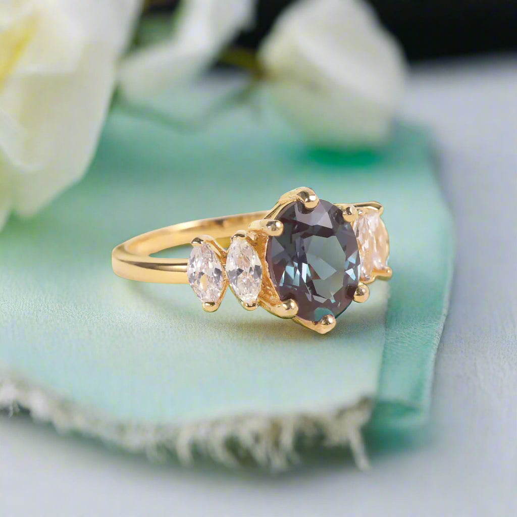Gold ring with a dark gemstone and smaller clear stones on a light background