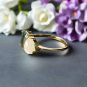 Gold ring with a green and white gemstone on a dark surface