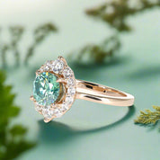 Gold ring with a green gemstone and diamond halo on a white background