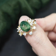 Gold ring with a green gemstone held between fingers against a blurred green background