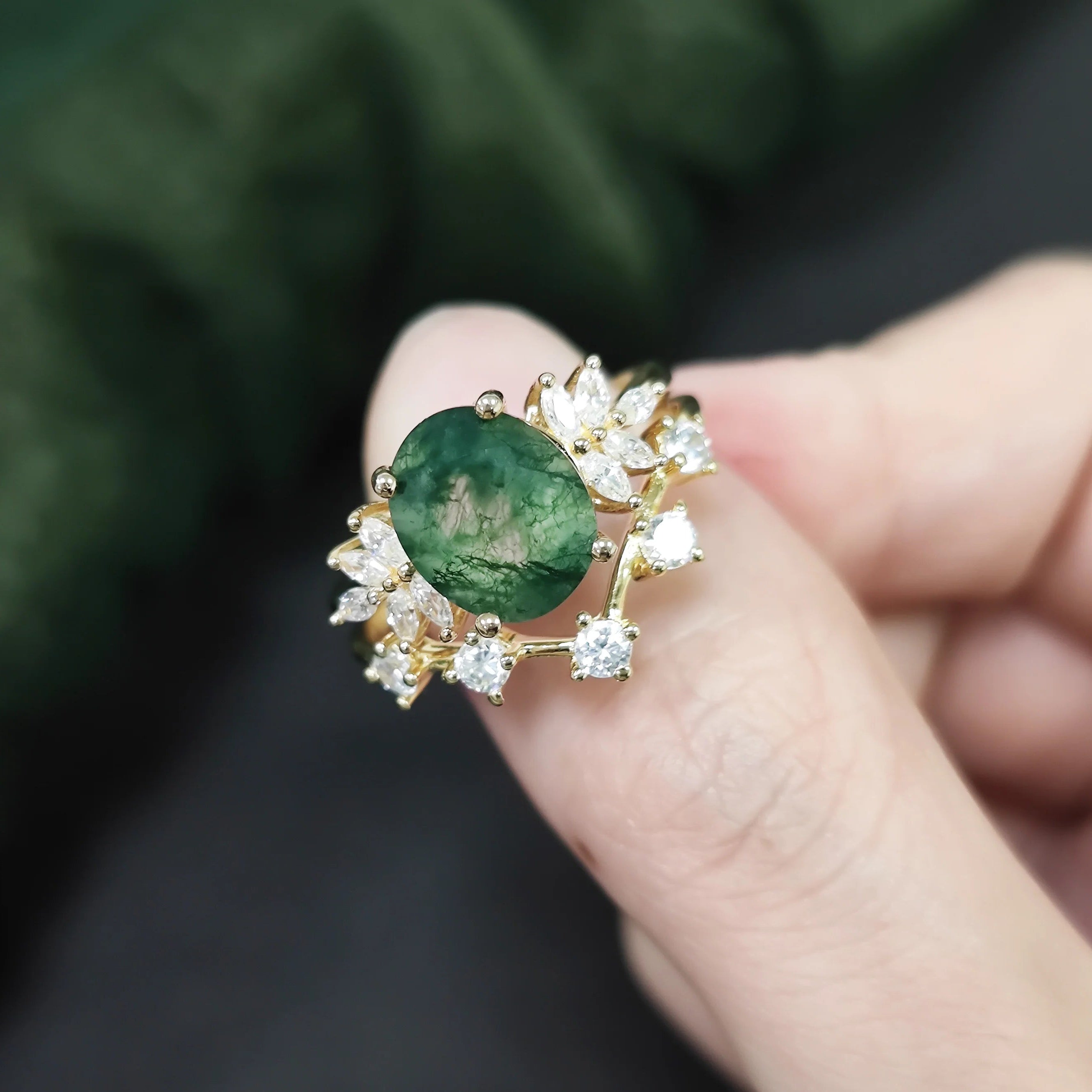 Gold ring with a green gemstone held between fingers against a blurred green background