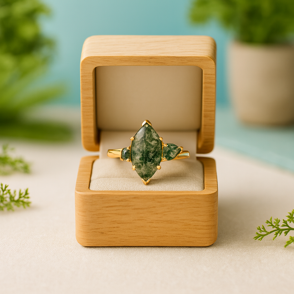 Gold ring with a green gemstone in a wooden box on a light surface with greenery.