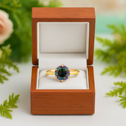 Gold ring with a green gemstone in a wooden box with a floral background