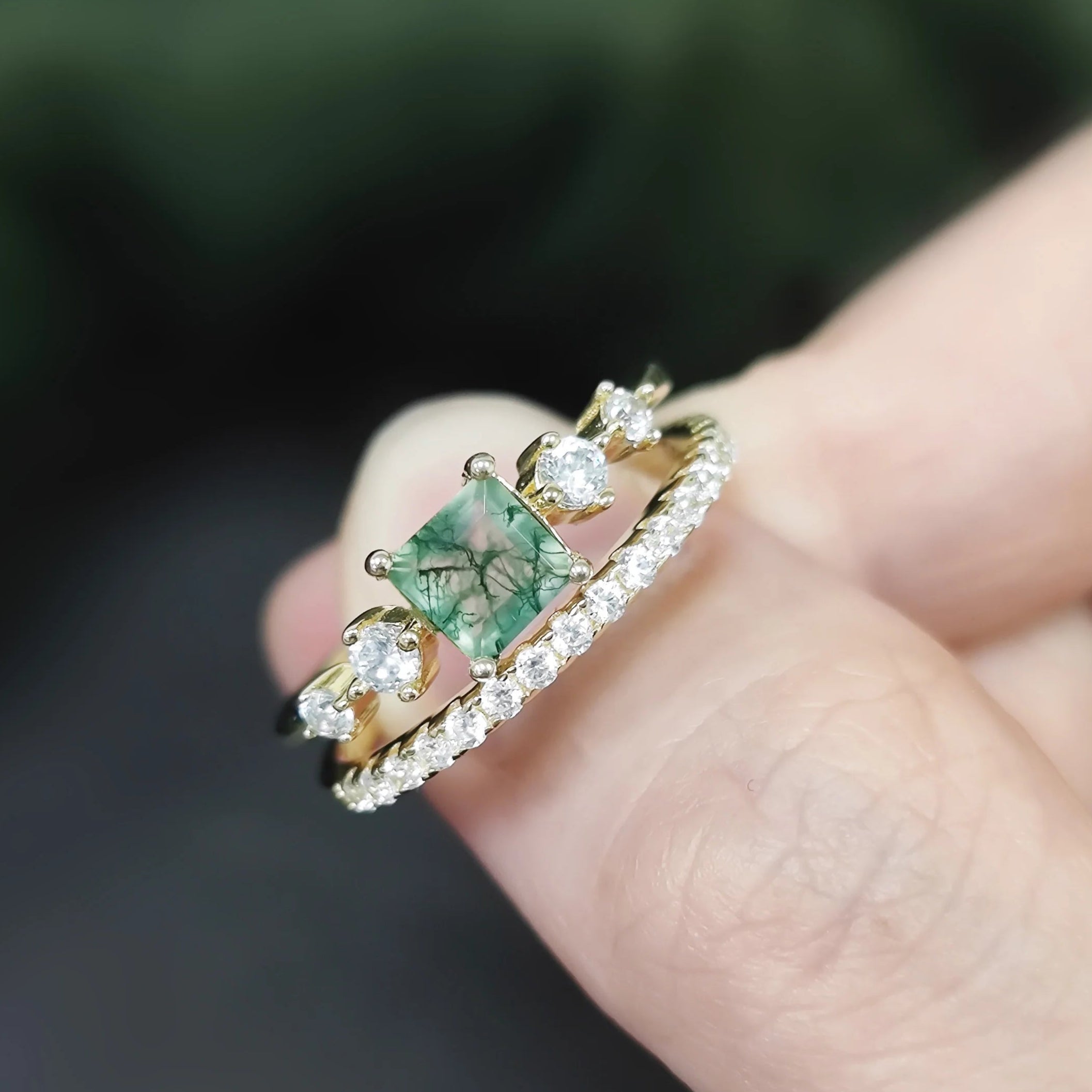 Gold ring with a green gemstone on a finger against a blurred background