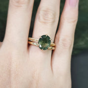 Gold ring with a green gemstone on a person's finger against a blurred background