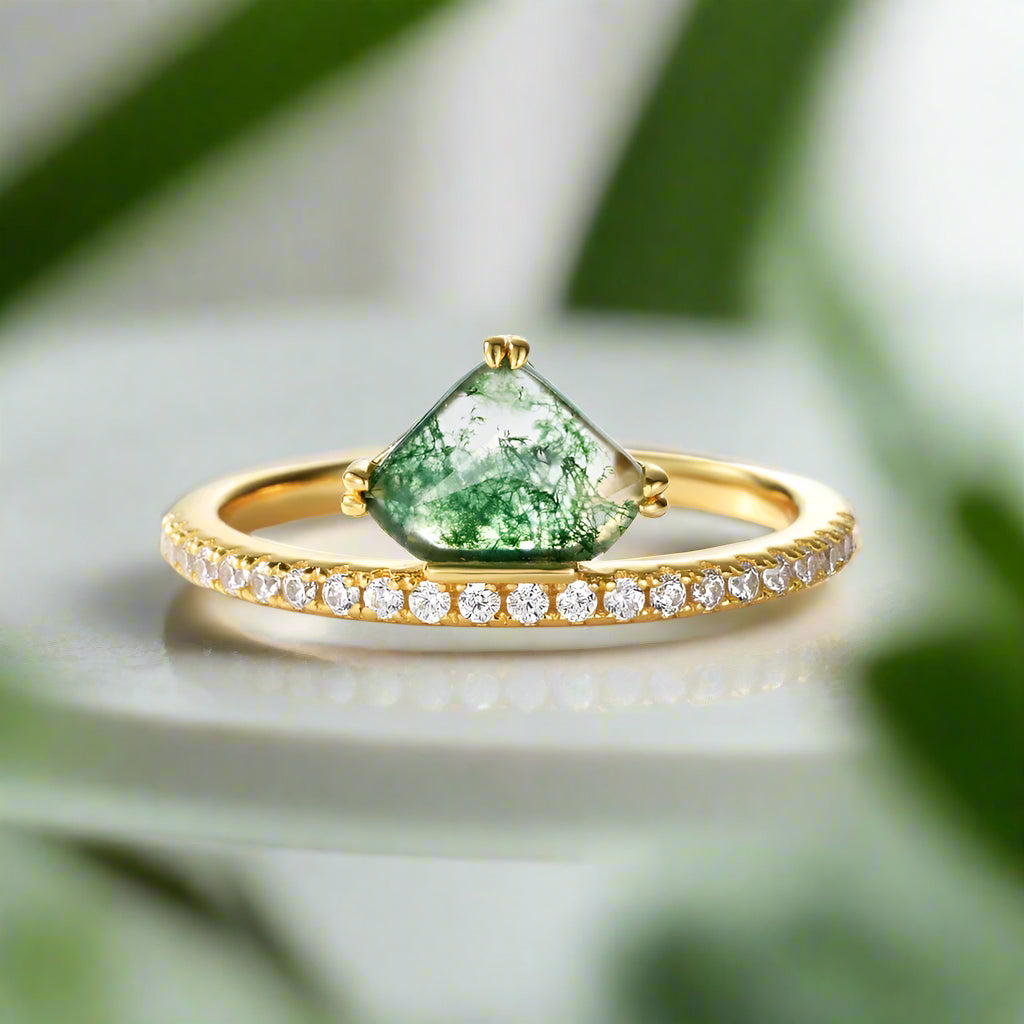 Gold ring with a green teardrop-shaped gemstone and small diamonds on a light gray background