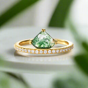 Gold ring with a green teardrop-shaped gemstone and small diamonds on a light gray background