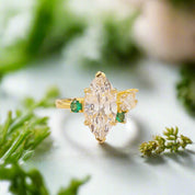 Gold ring with a large diamond and smaller emeralds on a light background with yellow petals.