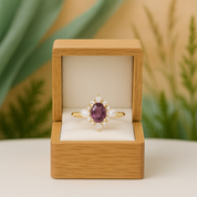 Gold ring with a purple gemstone in a wooden box against a natural background