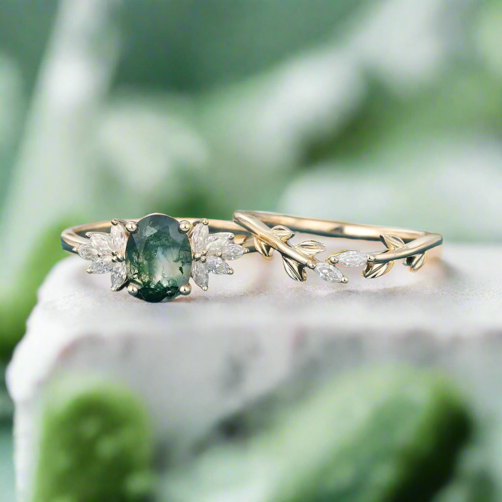 Gold ring with green gemstone and leaf design on a blue surface with dried flowers in the background