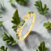 Gold ring with green gemstones and clear stones on a white background