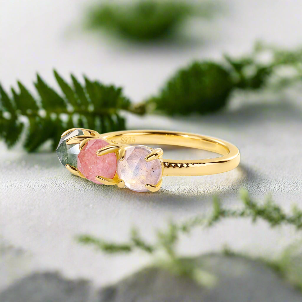 Gold ring with three colorful gemstones on a light gray background