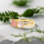 Gold ring with three colorful gemstones on a light gray background