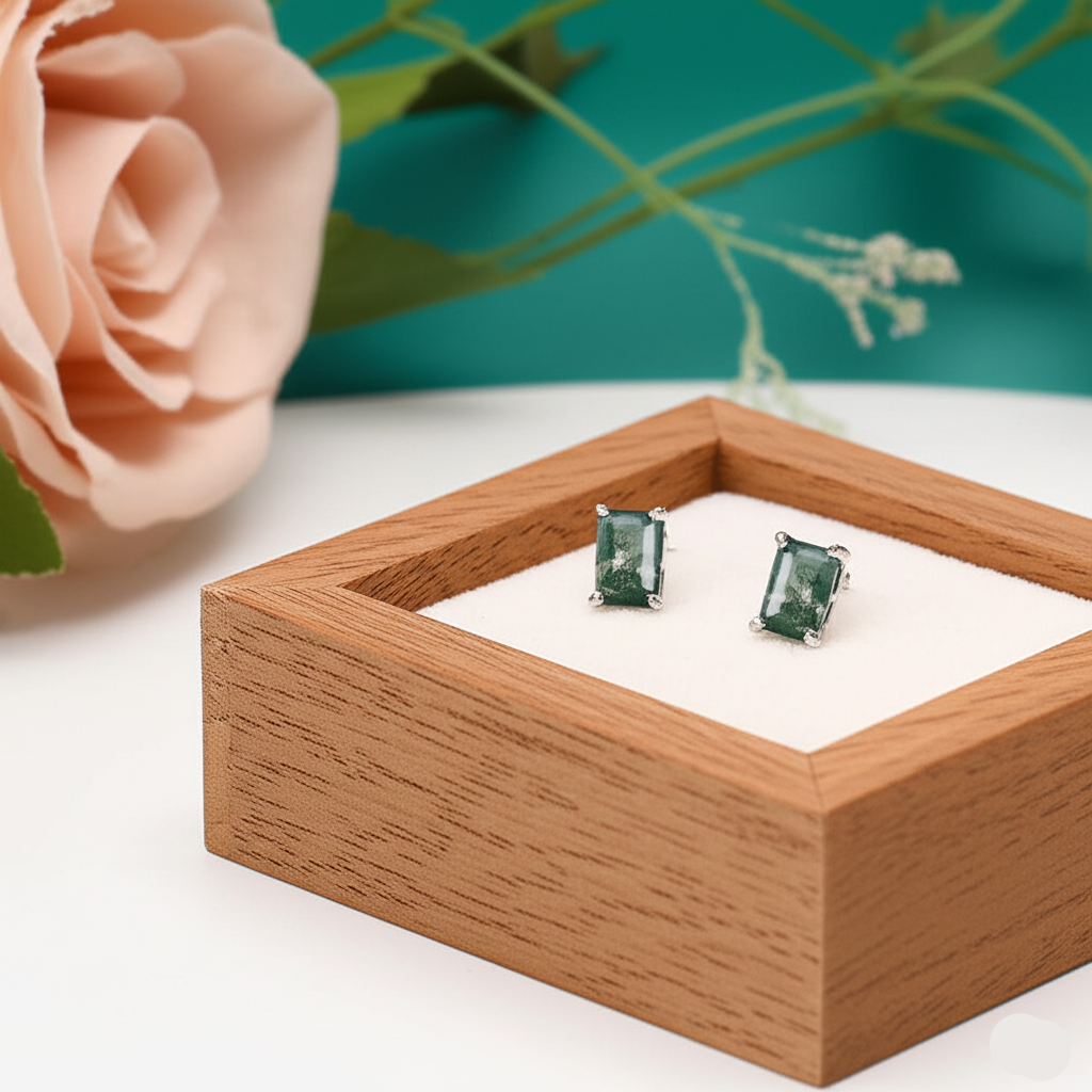 Green gemstone earrings in a wooden box with a rose in the background