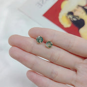 Green gemstone stud earrings held between fingers with a blurred background