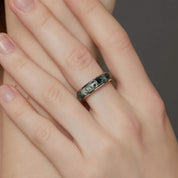 Hand wearing a ring with a dark band design, against a neutral background.
