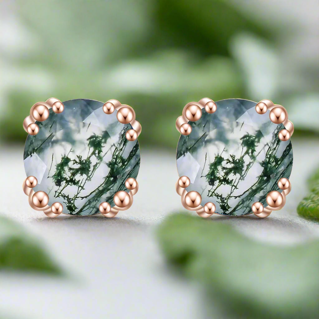Heart-shaped earrings with green gemstones and rose gold accents on a white background