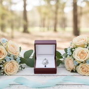 Jewelry box with a heart-shaped pendant surrounded by flowers in a forest setting