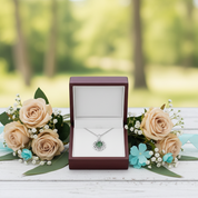 Jewelry box with a necklace inside, surrounded by flowers on a wooden surface with a blurred natural background